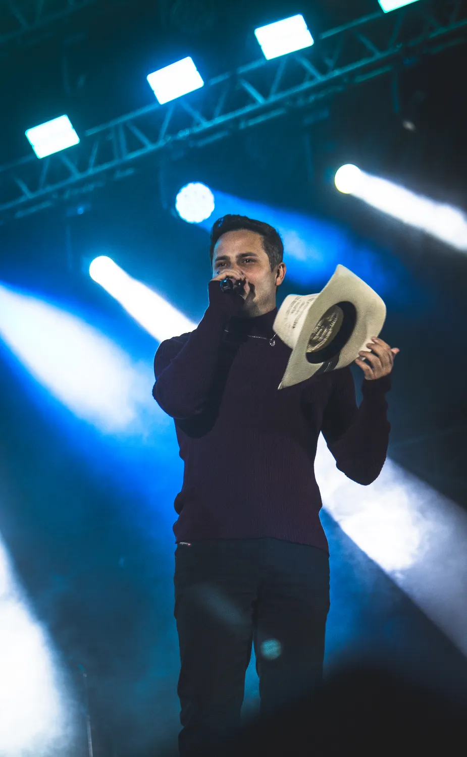 Cantor com chapéu segurando o microfone sob a luz azul do palco — Rodeio Fest 2026, 07.08